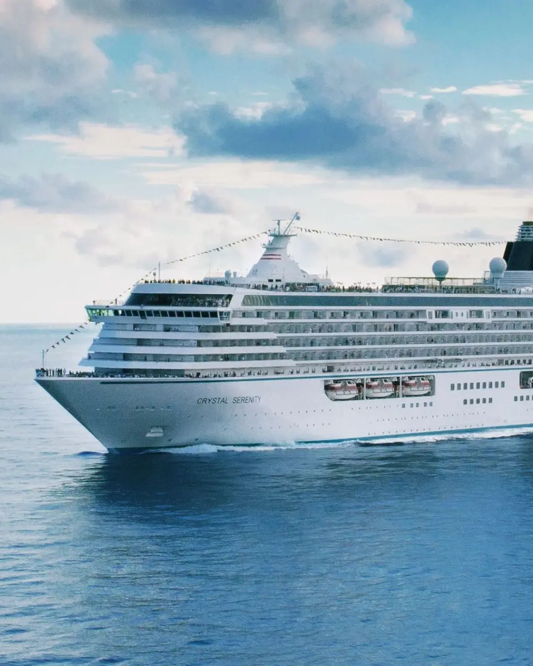White cruise ship, Crystal Cruises Serenity sailing on calm blue water under a cloudy sky