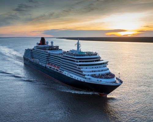 Cunard Queen Victoria cruise ship sailing at sunset on calm water, with a warm orange sky