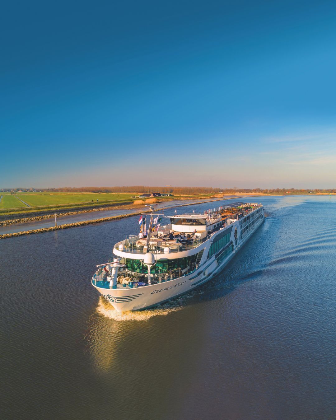 Large white river cruise ship sailing on calm water under a clear blue sky.
