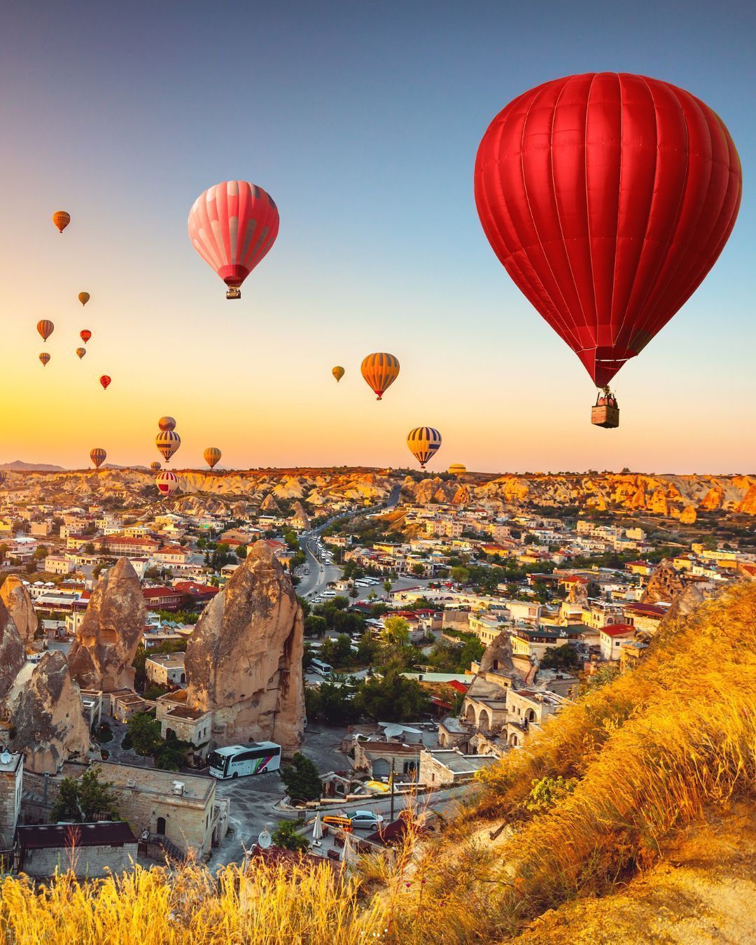 Hot air balloons over a rocky valley at sunrise, with a large red balloon in the foreground.