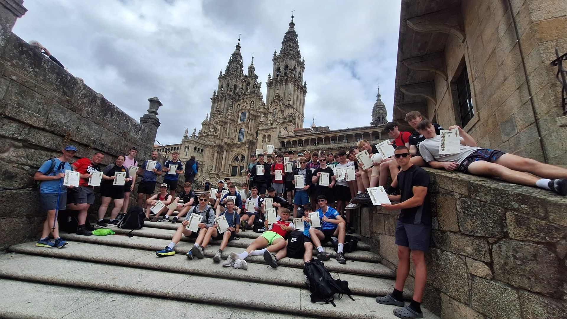 Large group posing on stone steps before the Santiago de Compostelala cathedral with twin spires, in an outdoor plaza.