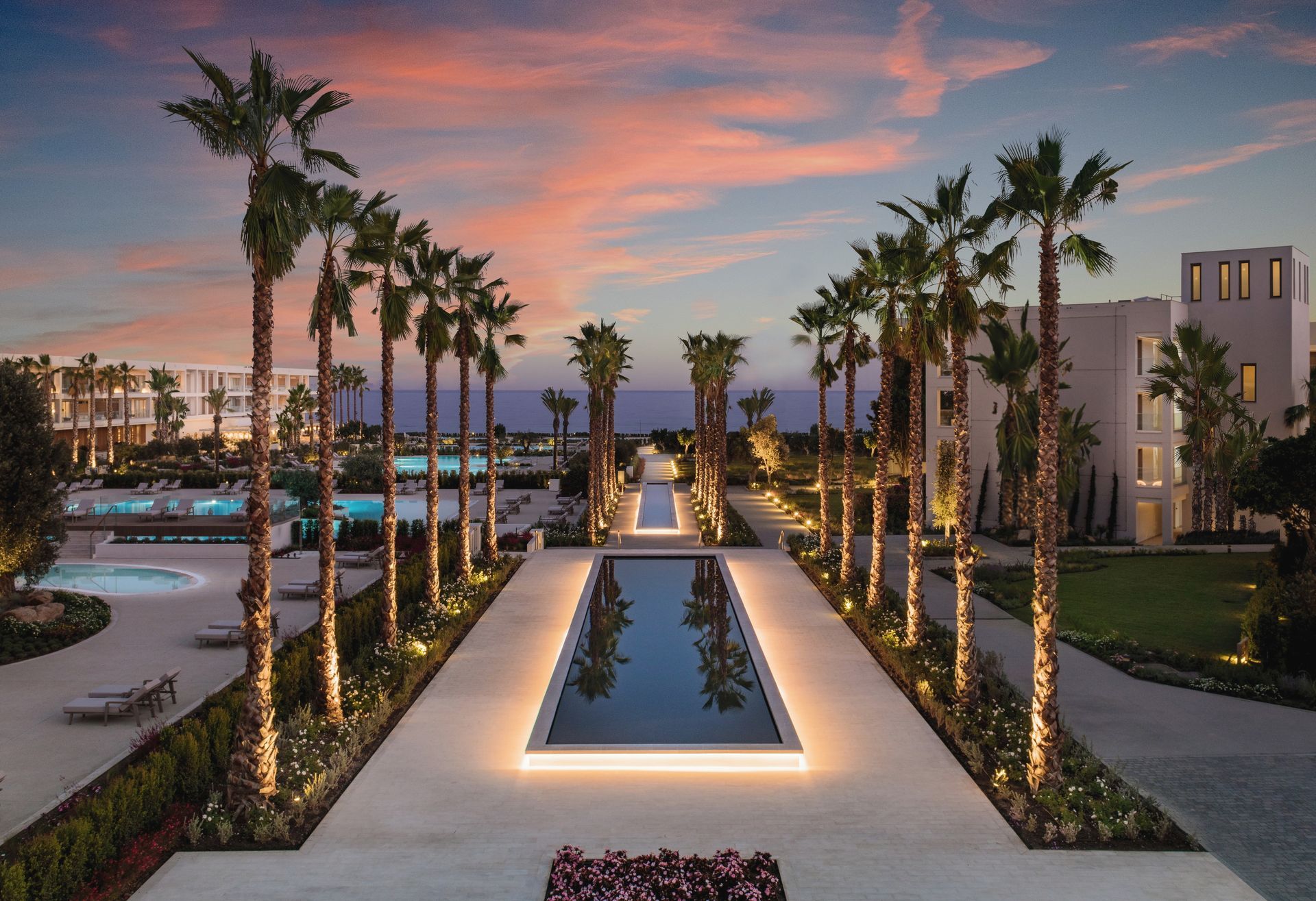 Palm-lined resort courtyard at dusk with a reflecting pool and warm pathway lights