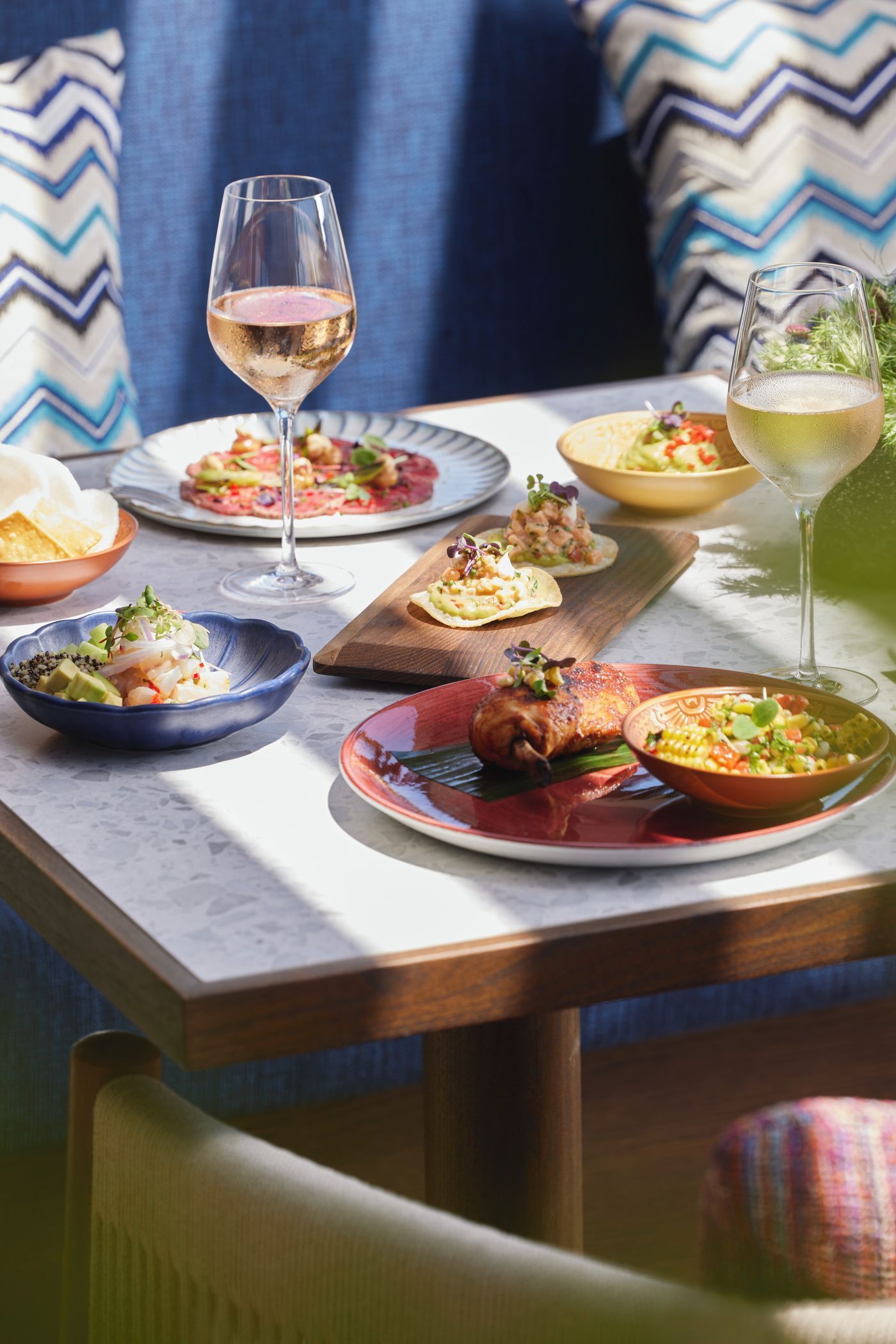 Outdoor dining table with wine, plated meals, and snacks in sunlight