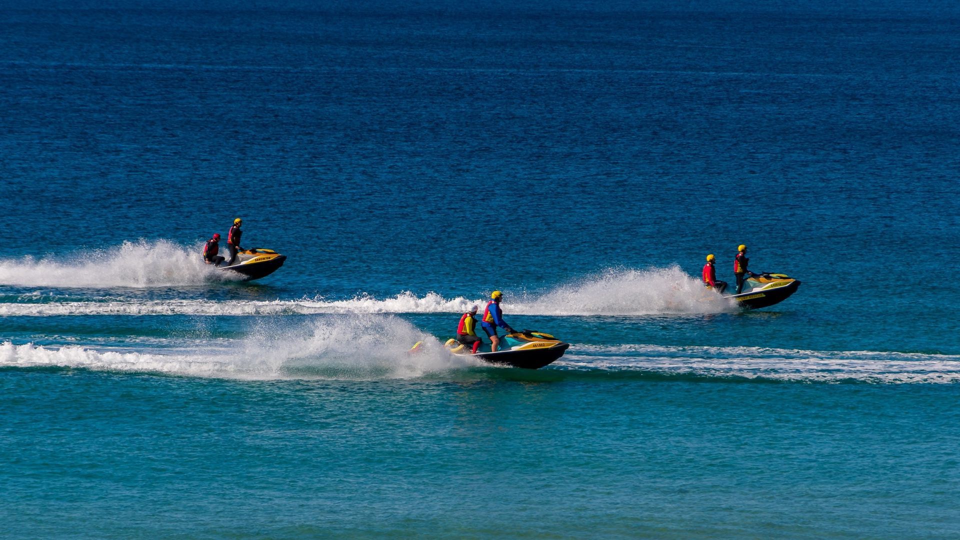 Three jet skis speeding across blue water, leaving white wakes behind them