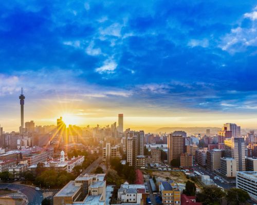 Johannesburg skyline at sunrise with golden light, blue sky, and a tall tower on the left