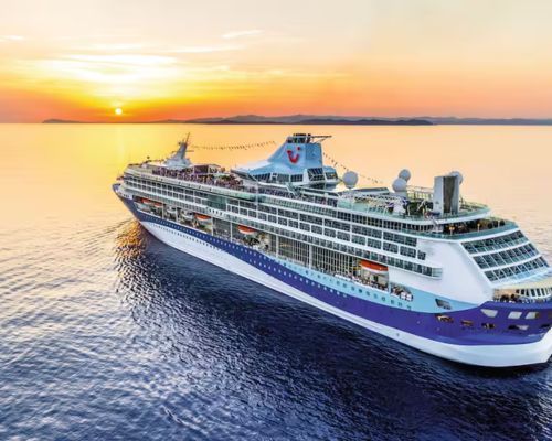 Marella Discovery cruise ship sailing on calm water at sunset, with a golden sky and distant horizon.