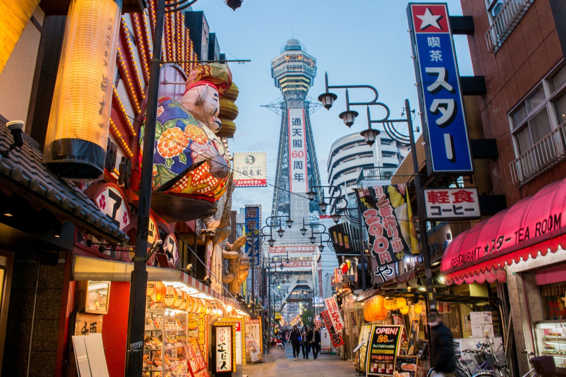 A busy street in Osaka Tsutenkaku
with a tower in the background.