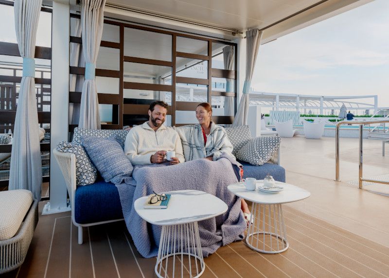 Two people relaxing on a blue sofa in a rooftop lounge deck on a Princess cruise ship