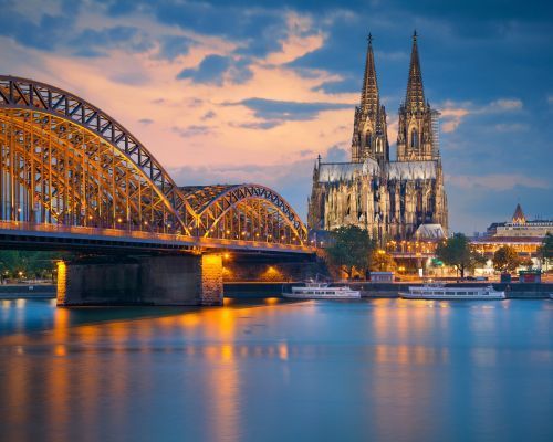 Cologne Cathedral and Hohenzollern Bridge glowing at sunset over the Rhine River