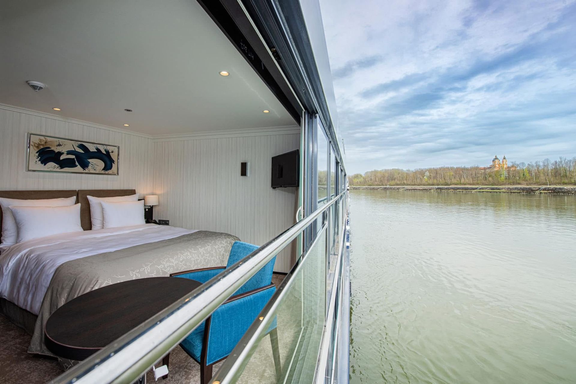 Modern bedroom with glass wall and balcony overlooking a calm river, Avalon Waterways