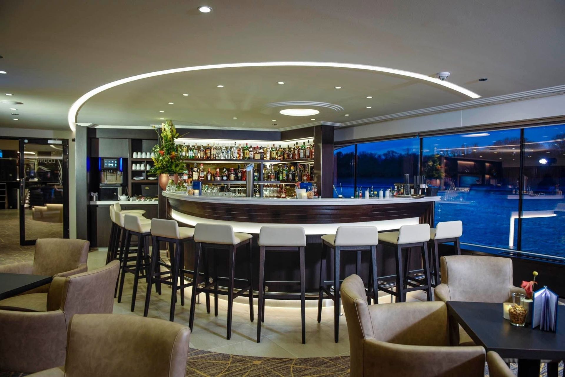 Modern lounge bar with curved white counter, high stools, and blue-lit windows overlooking the city, Avalon Waterways