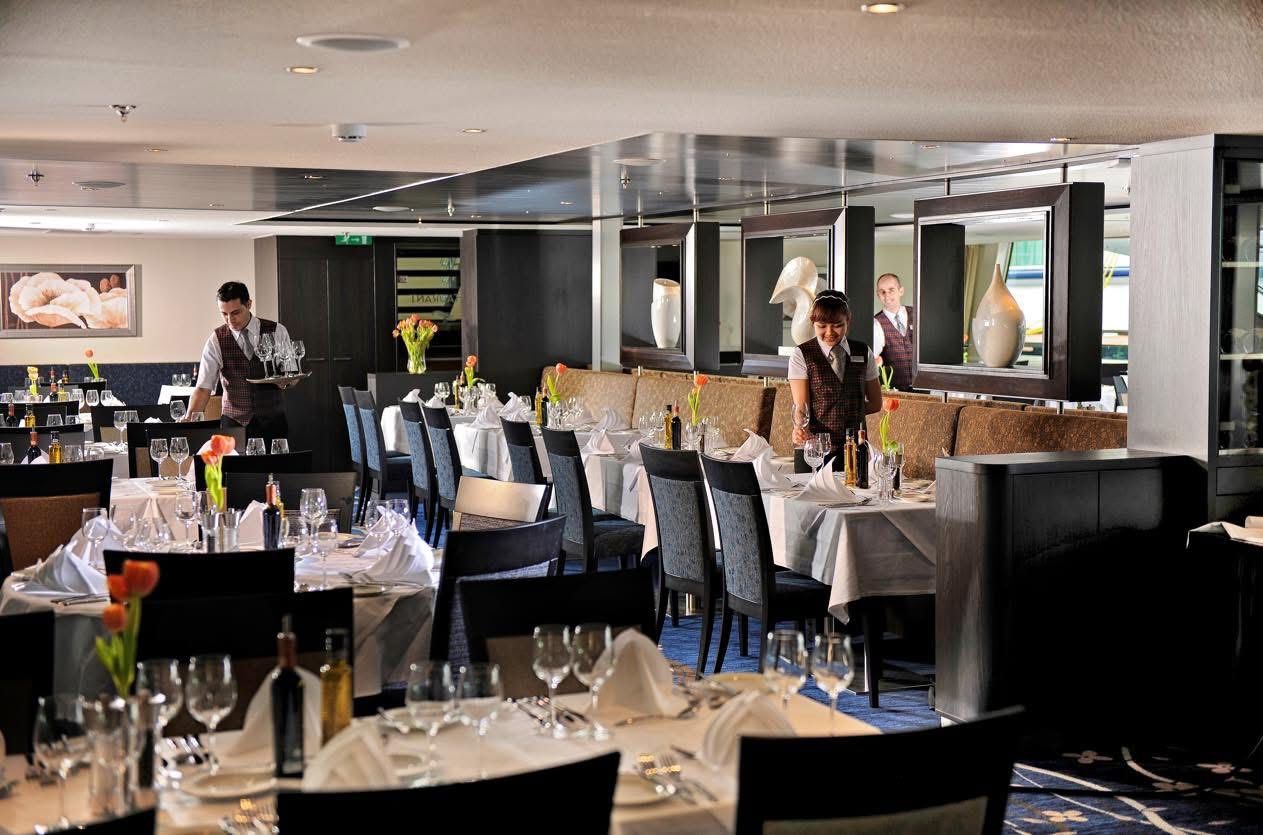 Elegant restaurant dining room with set tables, white linens, and a few people in the background, Avalon Waterways