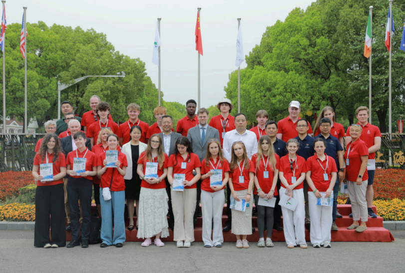 Group of irish students in red and white uniforms posing outdoors in front of flags and flower beds in China
