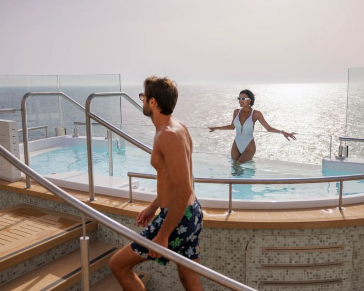 Silver Ray cruise ship two people in swimsuits near a pool at sunset, with ocean and railing in the background