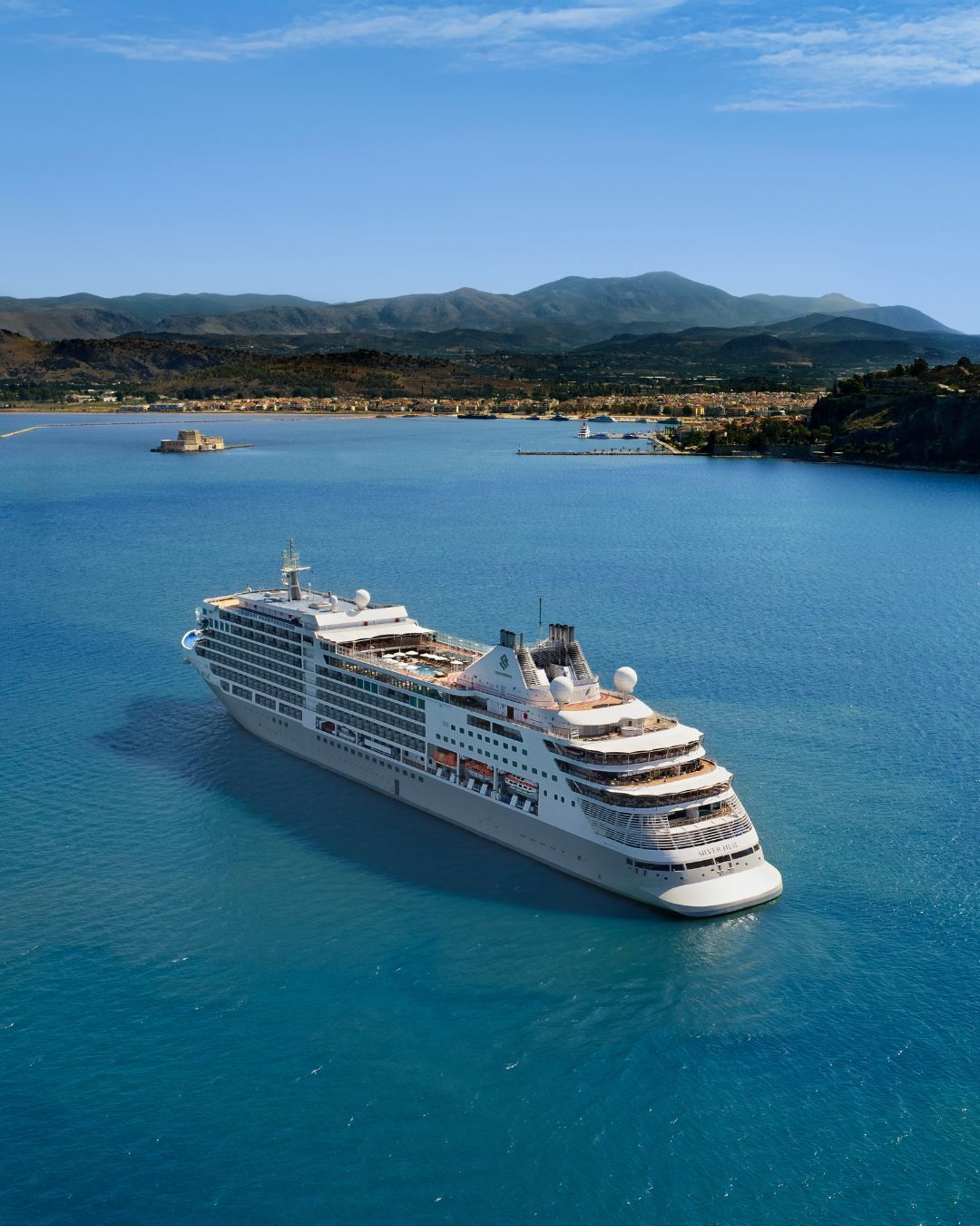 White cruise ship sailing on bright blue water near a mountainous tropical coastline