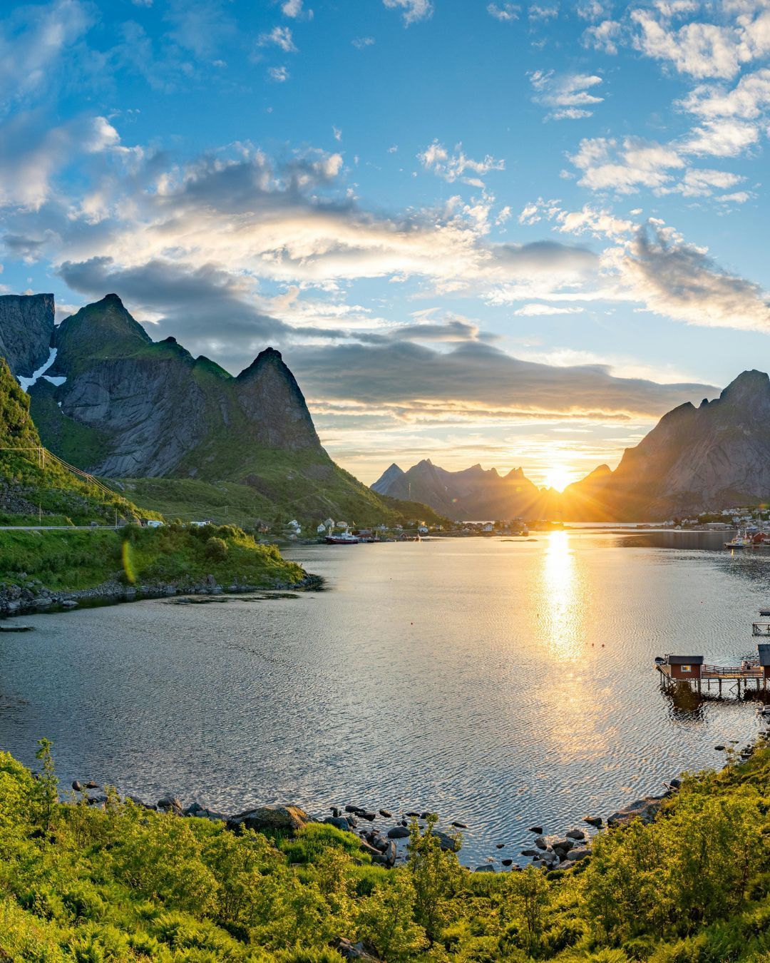 Sunset over a calm bay with mountains, clouds, and a glowing reflection on the water