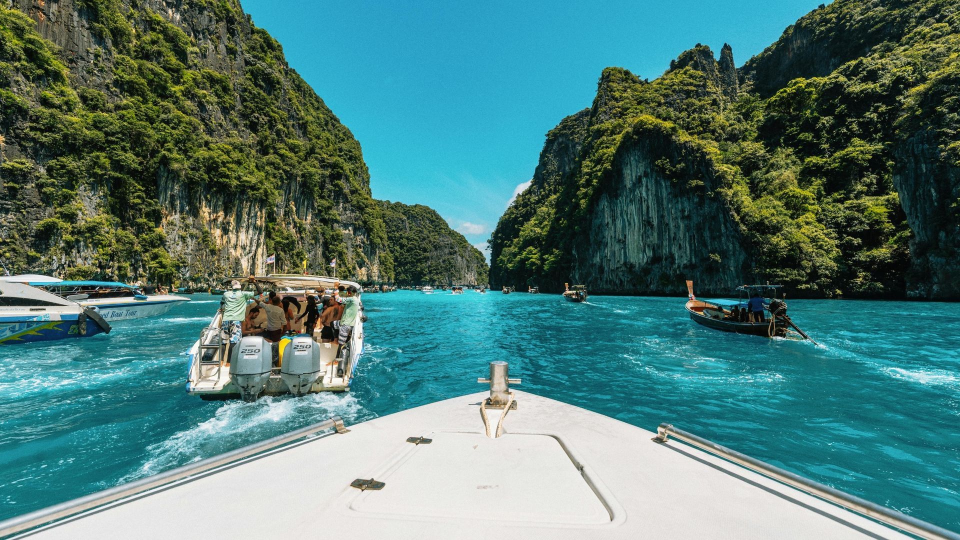 Speedboat on turquoise water approaching green limestone cliffs and a sunny tropical cove
