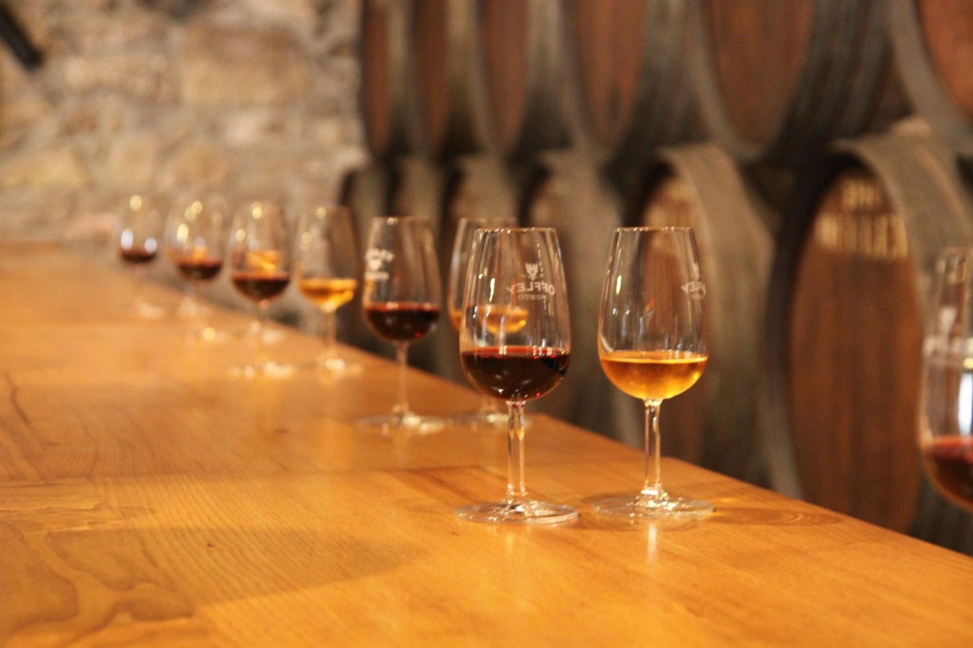 Rows of wine glasses on a wooden bar in a barrel-lined cellar in Douro, Porto