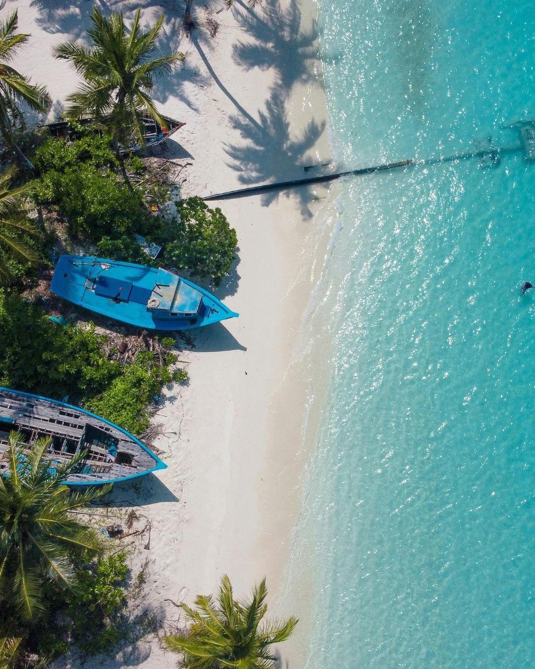 Aerial view of a tropical beach with turquoise water, palm trees, and small boats on white sand