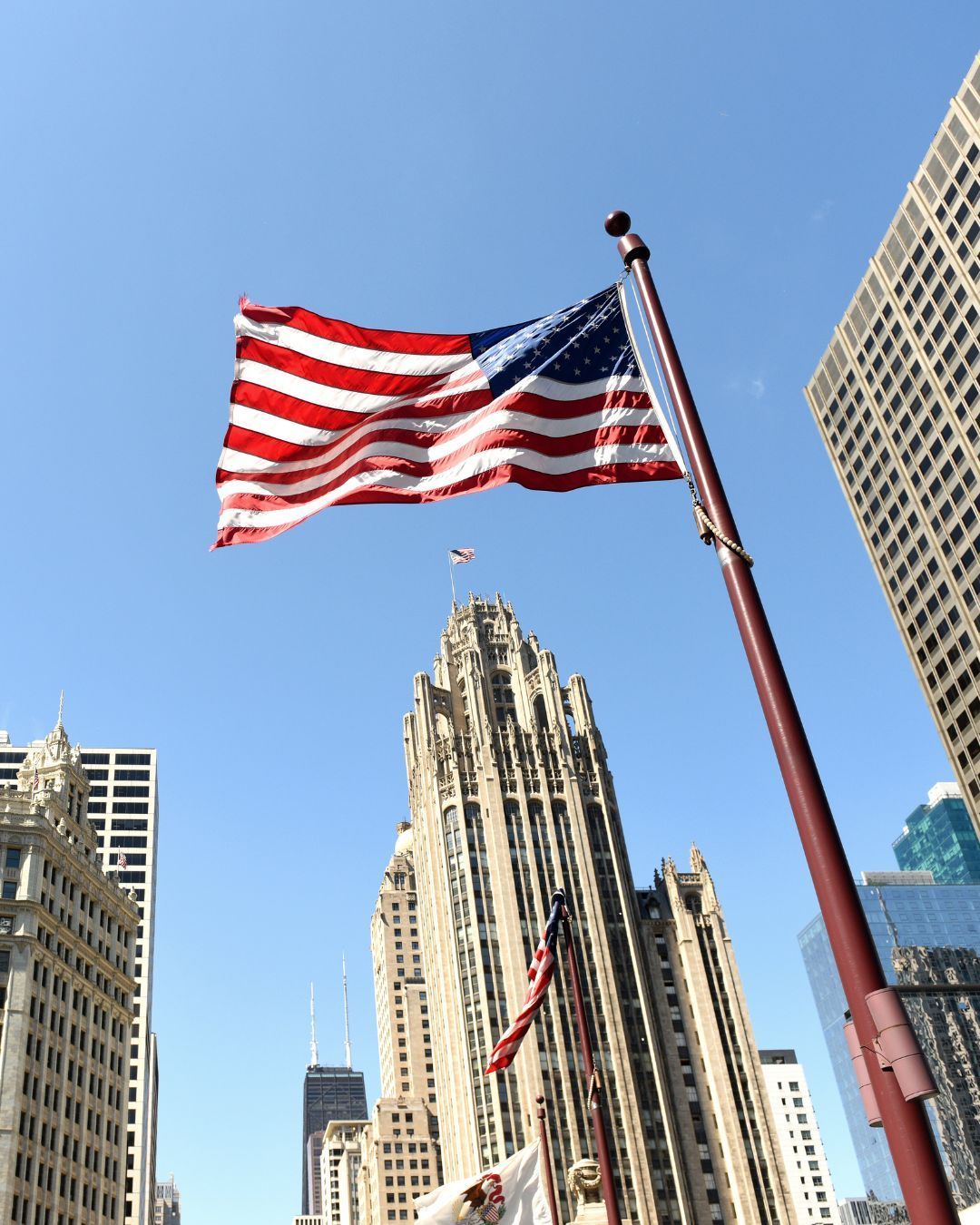 American flag waving beside a tall Art Deco skyscraper under a clear blue sky