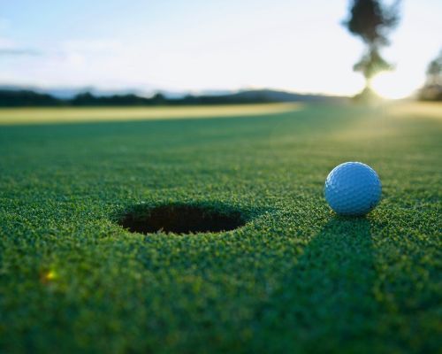 Golf ball beside hole on a green putting surface at sunrise