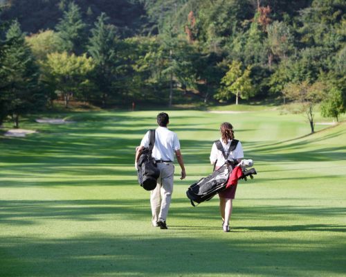 Two golfers walking down a green fairway with golf bags on their shoulders