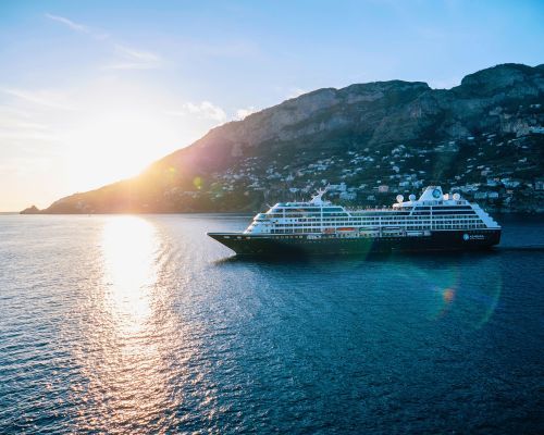 Azamara Pursuit on calm blue water beside a mountain at sunset