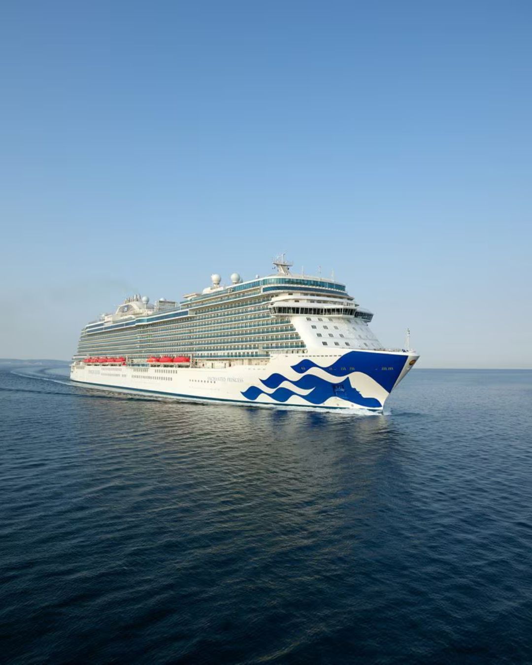 Large white cruise ship Enchanted Princess with blue wave design sailing on calm open water under a clear sky