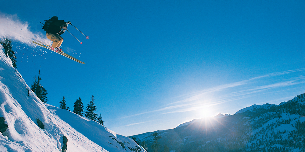 A person skiing doing a jump with a beautiful view of mountains covered in snow - Blog Post Barters Travelnet