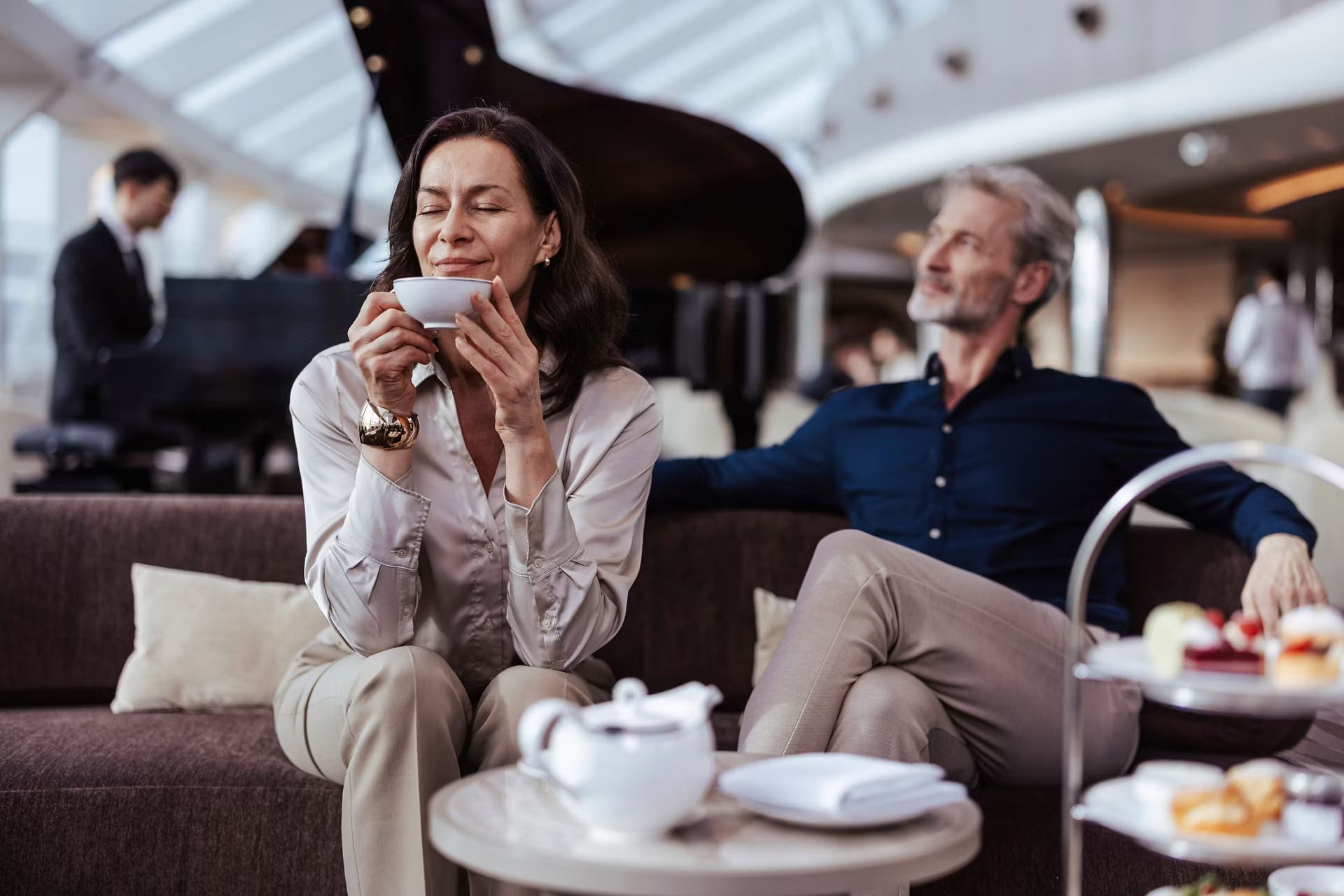 Woman smiling with coffee in a lounge while a man sits beside her near a tea service