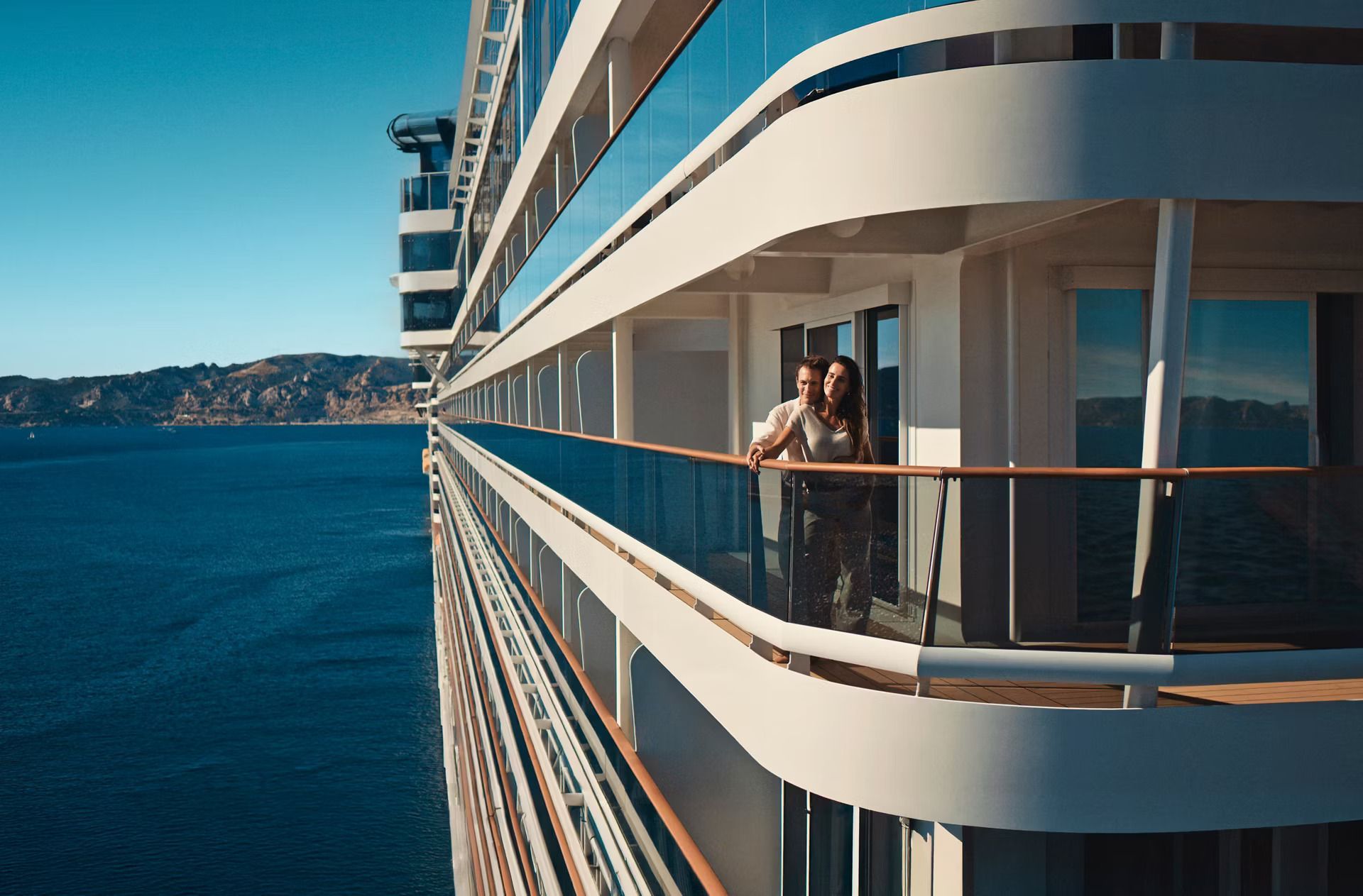 Cruise ship balcony overlooking blue water, with a person standing and taking a photo.