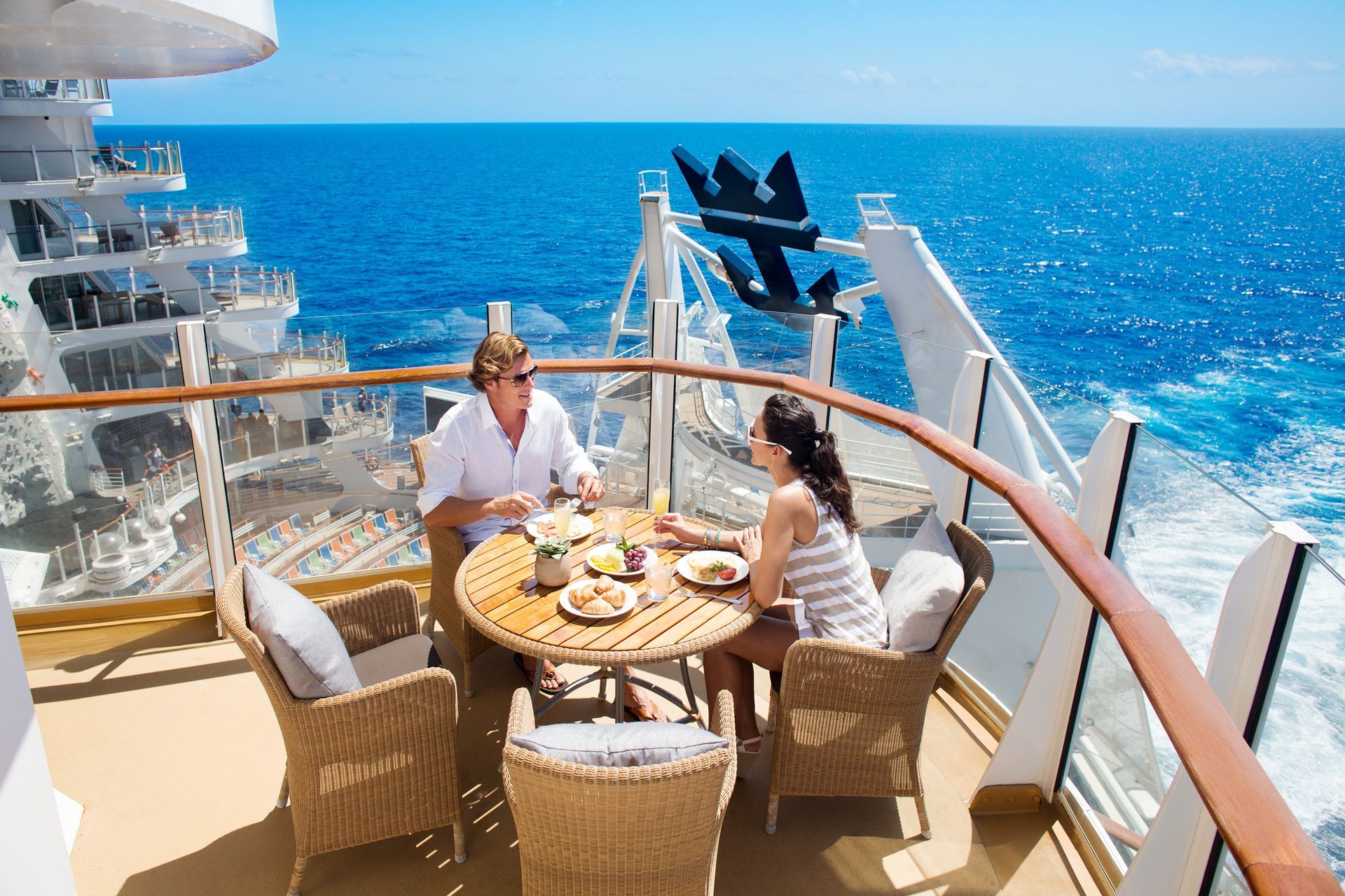 a man and a woman are sitting at a table on a balcony on a cruise ship.Barter'sTravelnet
