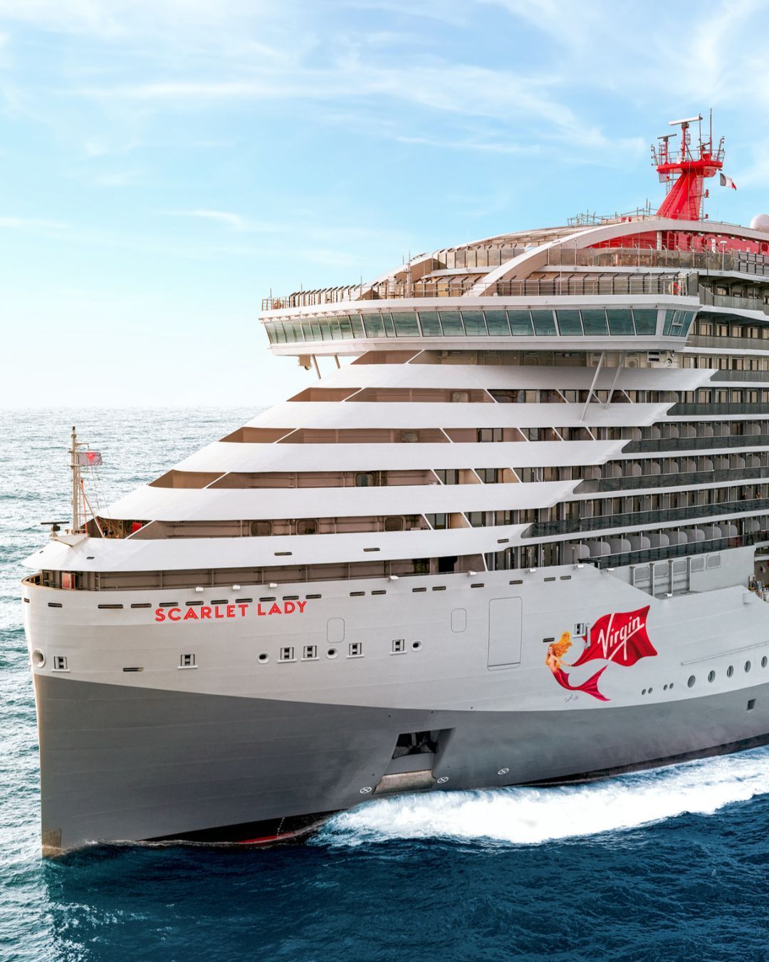 Large white cruise ship, Virgin Scarlet, at sea, with red funnel and bow, cutting through blue water