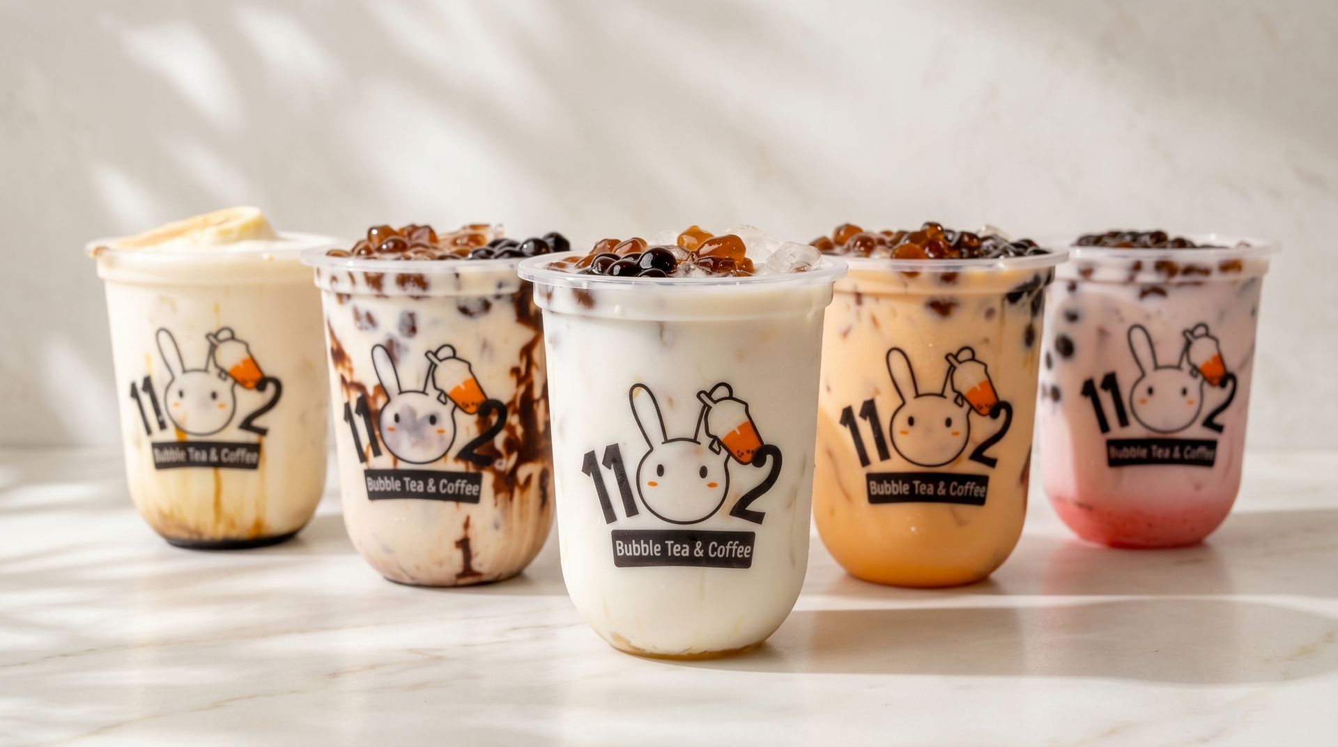 Five assorted milk tea cups with bunny logos, toppings, and colorful drinks on a bright table