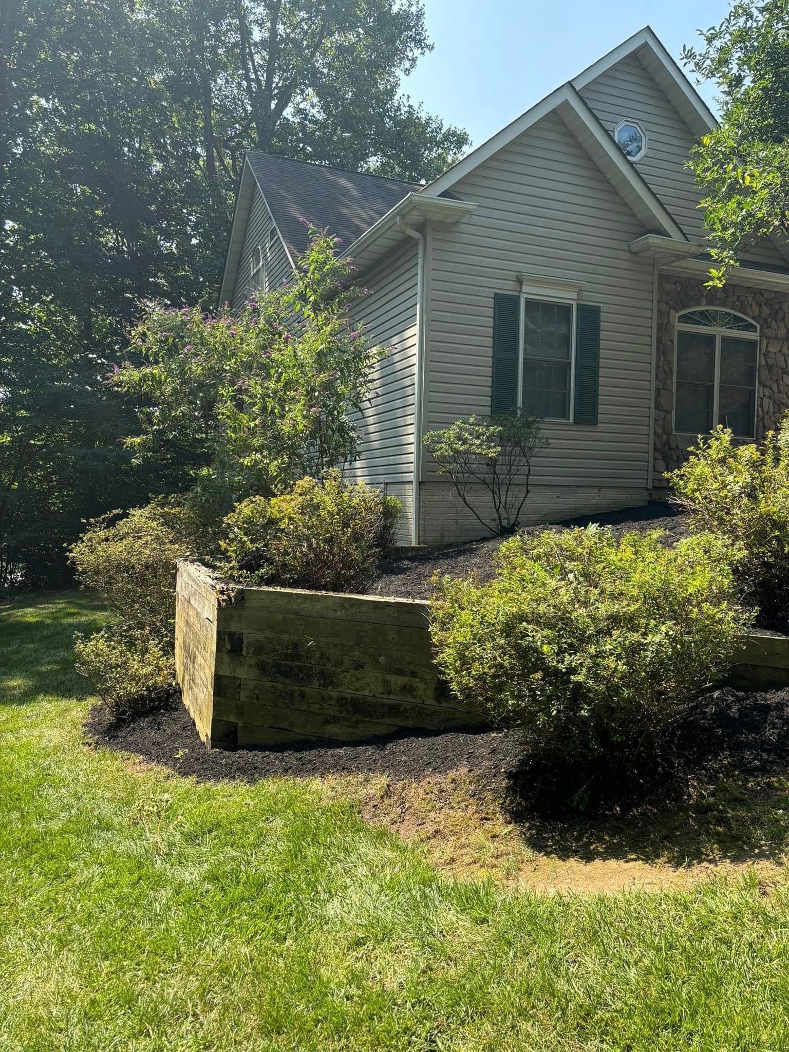 Small white house with a steep roof, surrounded by green bushes and lawn in bright sunlight