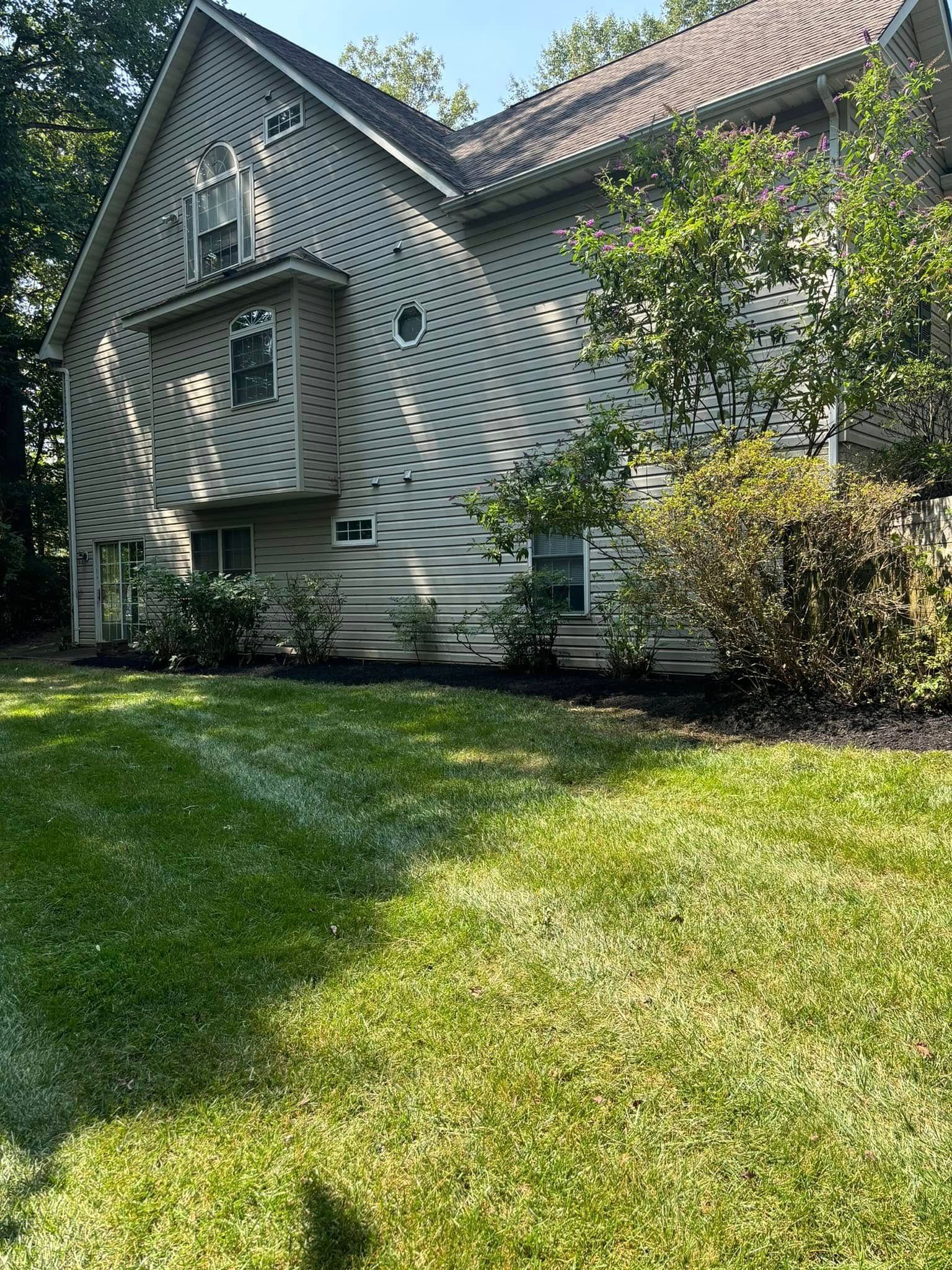 Sunlit house with gray siding and a lush green lawn, surrounded by trees.
