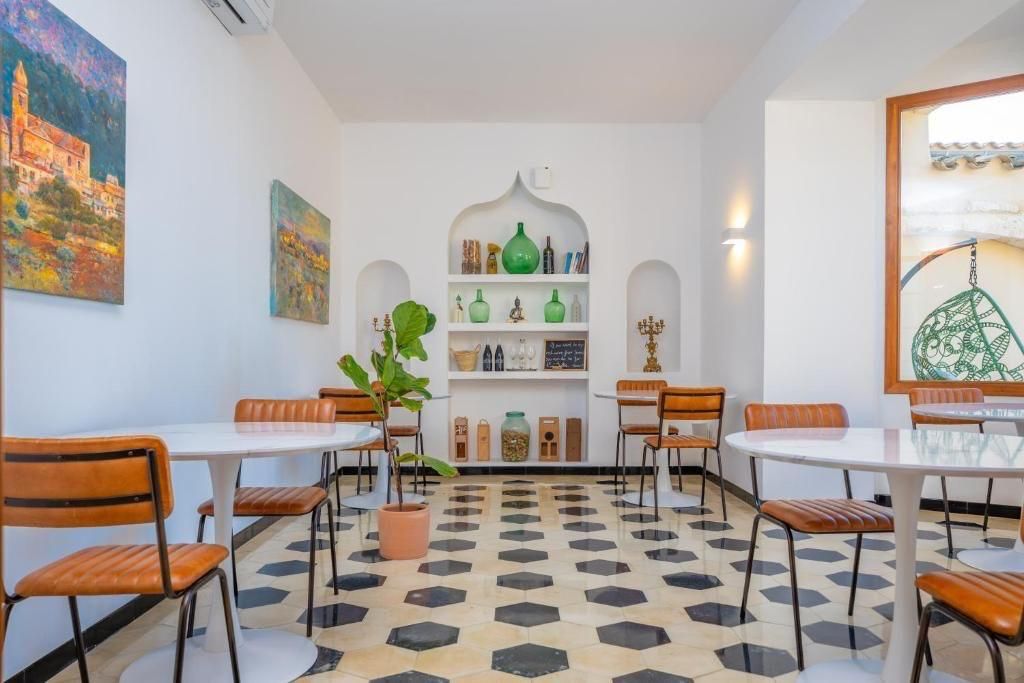 Interior de cafetería con paredes blancas, suelo estampado, mesas redondas y sillas de cuero marrón.