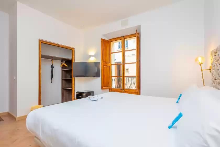 Dormitorio con cama grande, banco, mesita de noche y luces de pared.