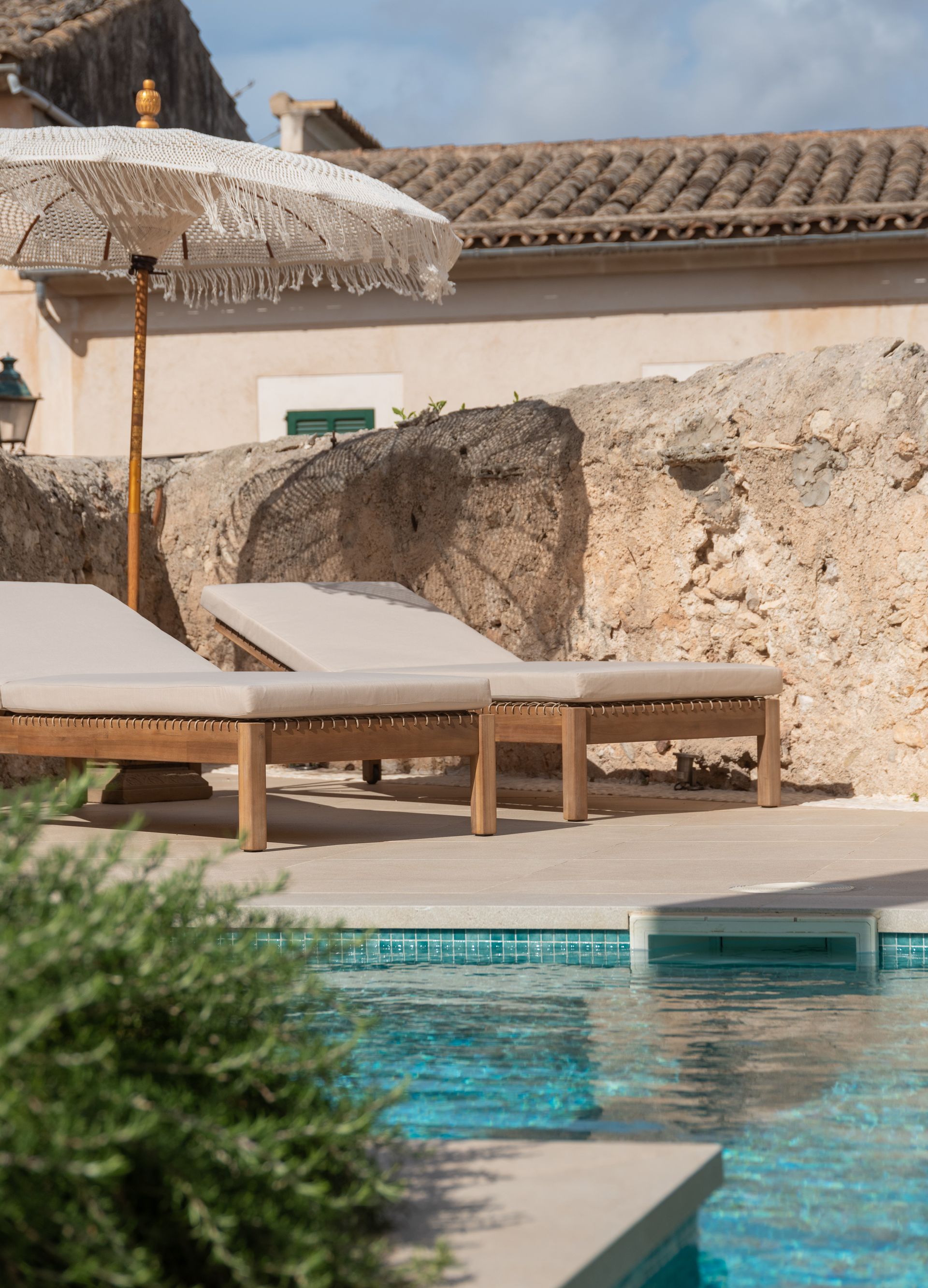 Hay dos tumbonas y una sombrilla al lado de una piscina.