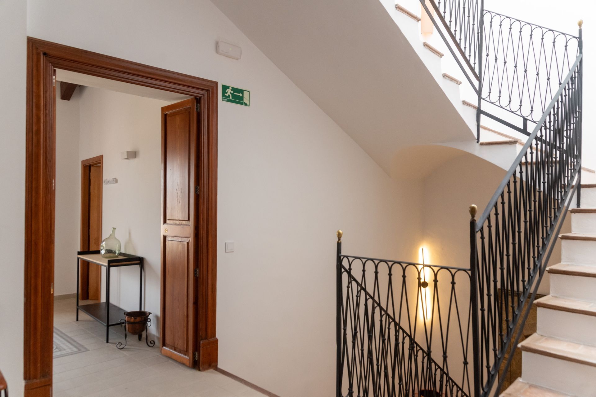 Una escalera con barandilla de hierro forjado y una señal de salida verde en la pared.