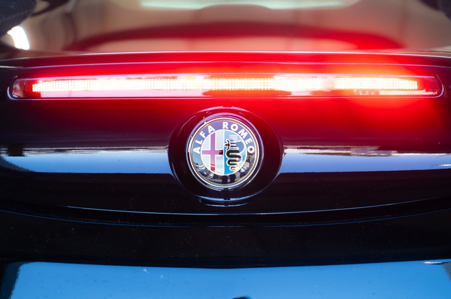 Close-up of an Alfa Romeo car's rear with glowing red brake light and emblem.
