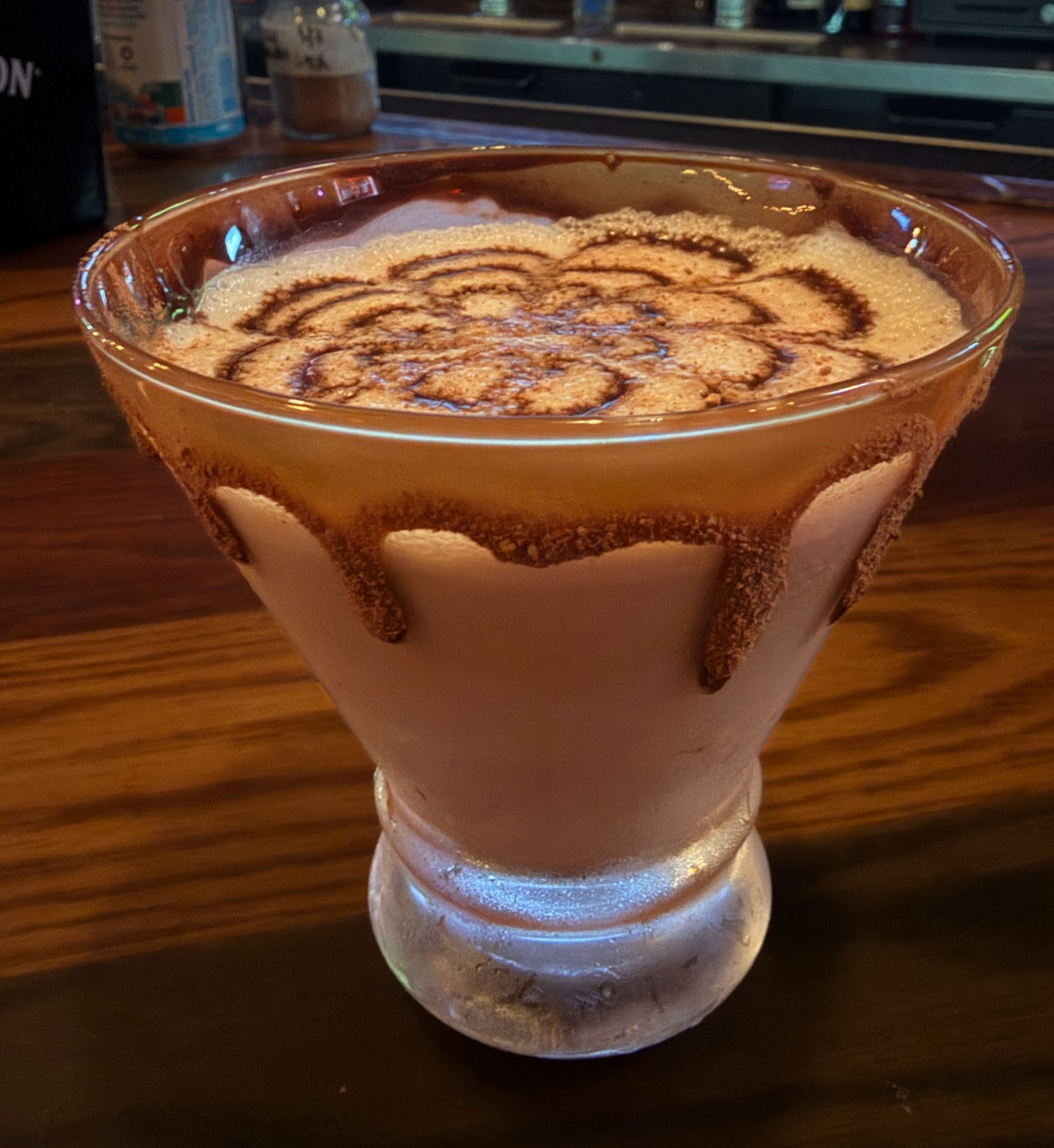 Chocolate martini in a glass with a cocoa swirl on top, sitting on a wooden bar.