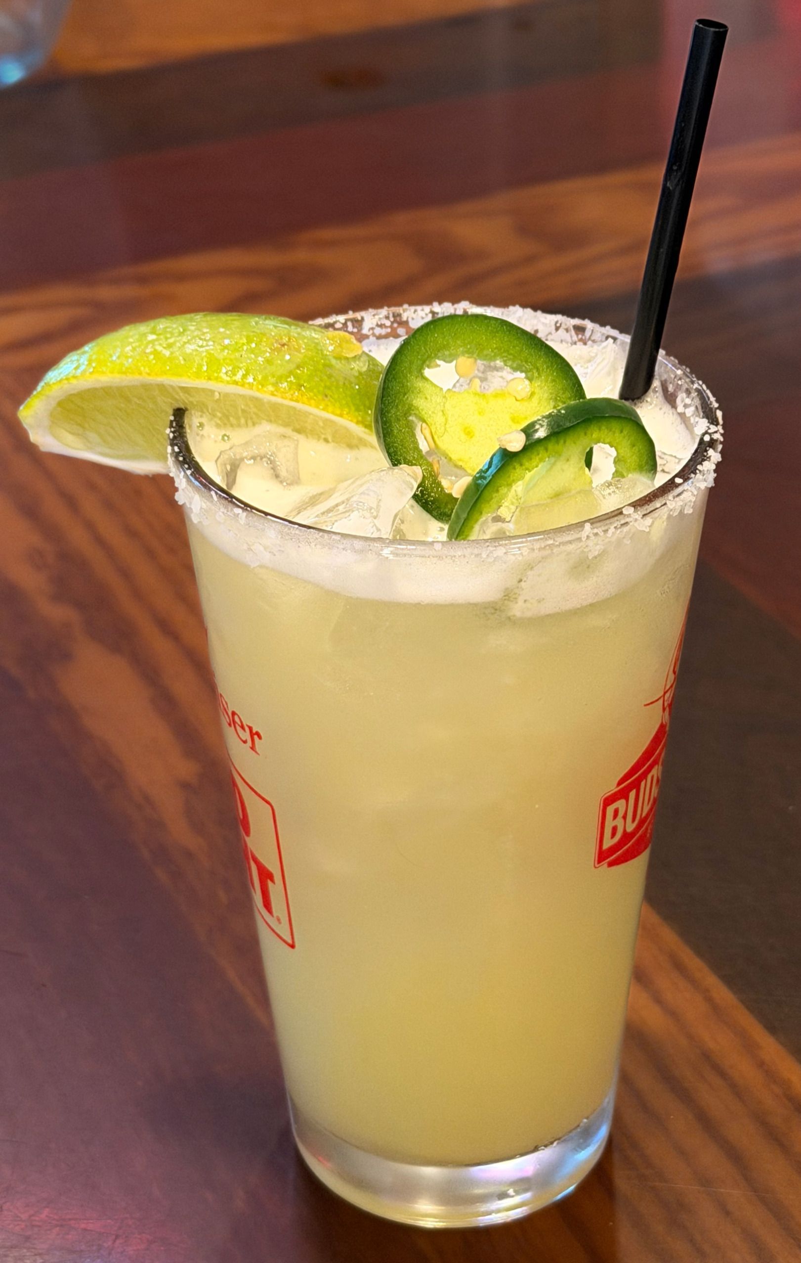 Tall pale cocktail with lime wedges and a straw on a table