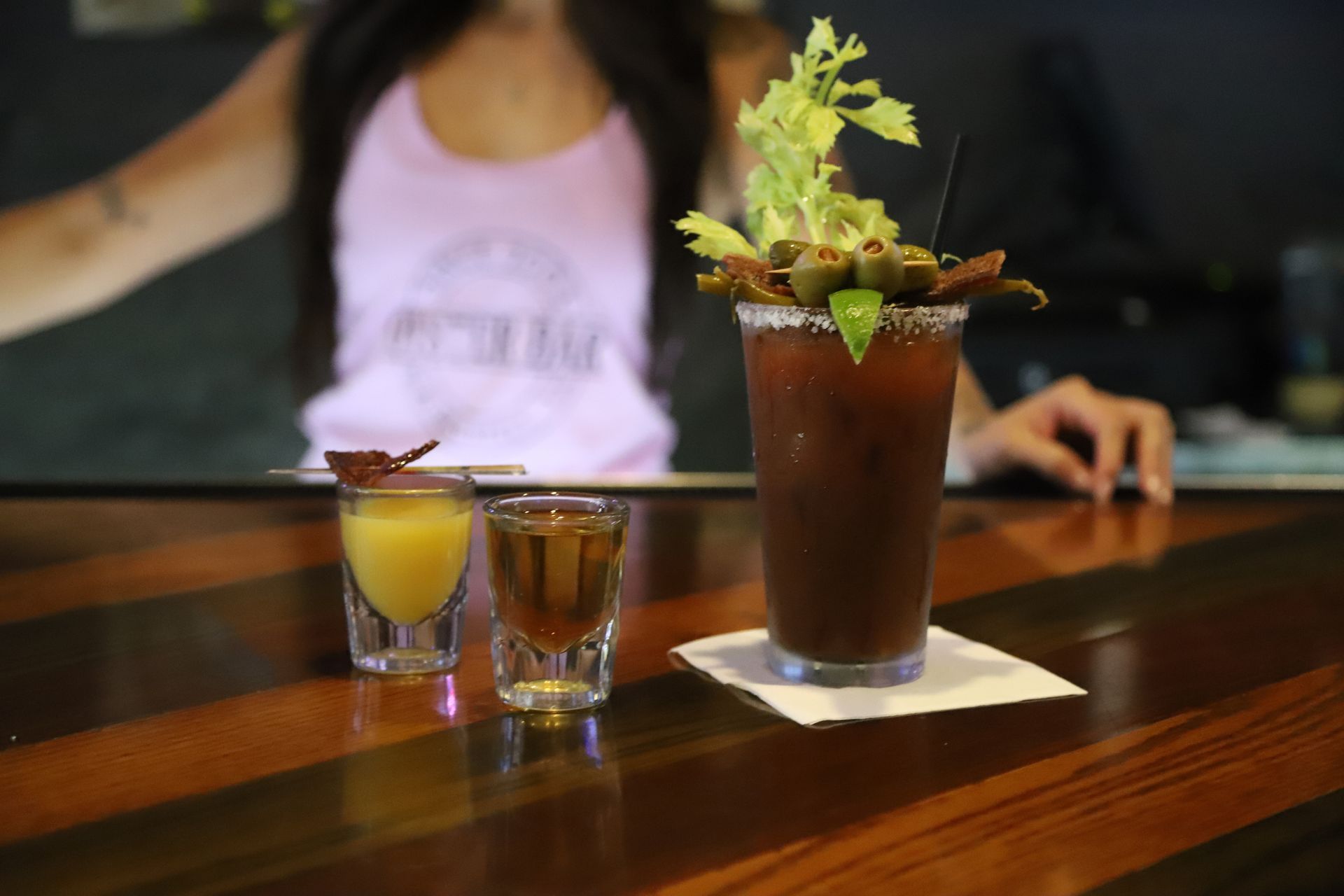 Bartender with a Bloody Mary cocktail, accompanied by two shots, on a bar.
