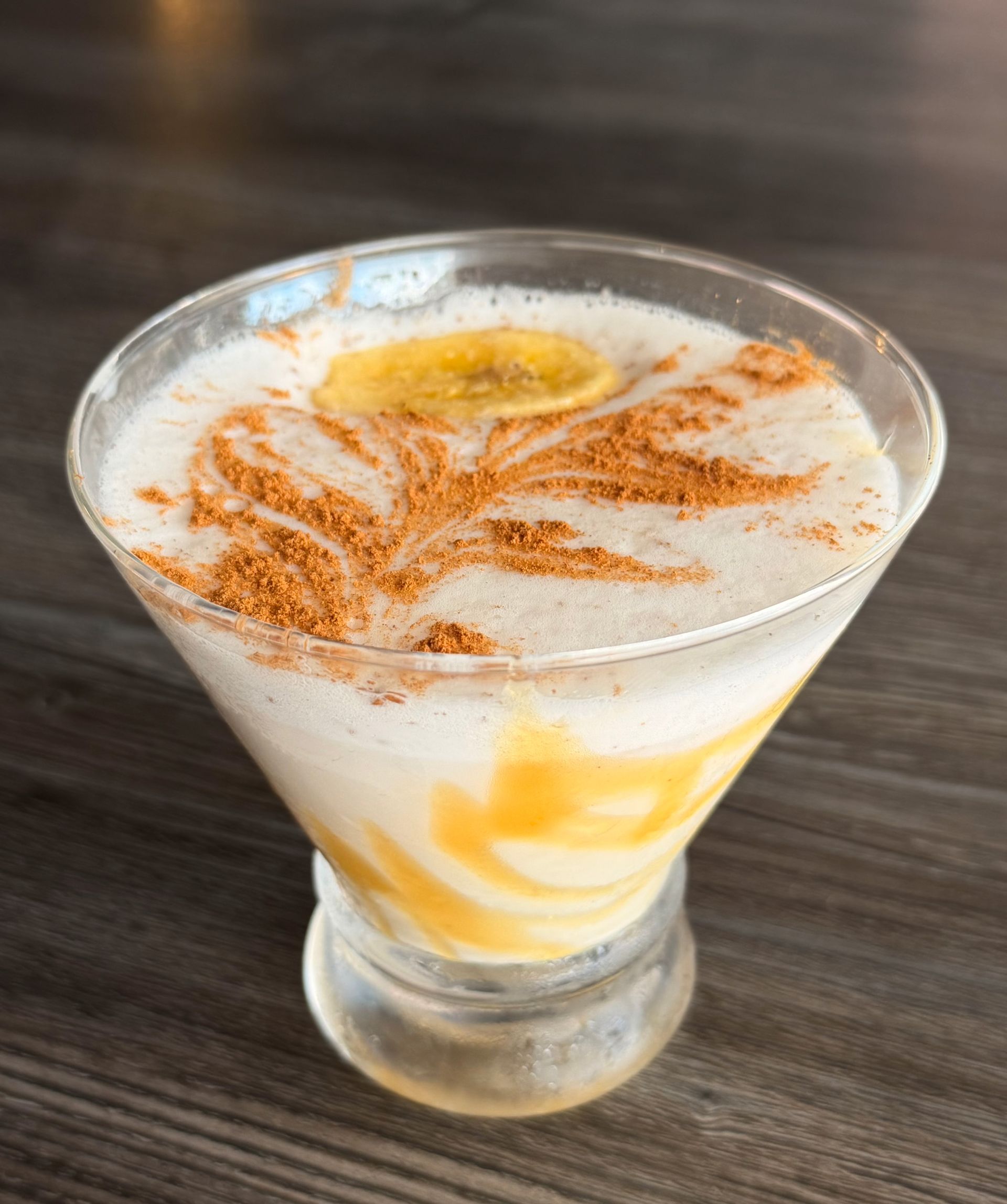 Glass of creamy dessert drink topped with cinnamon and honey on a dark table