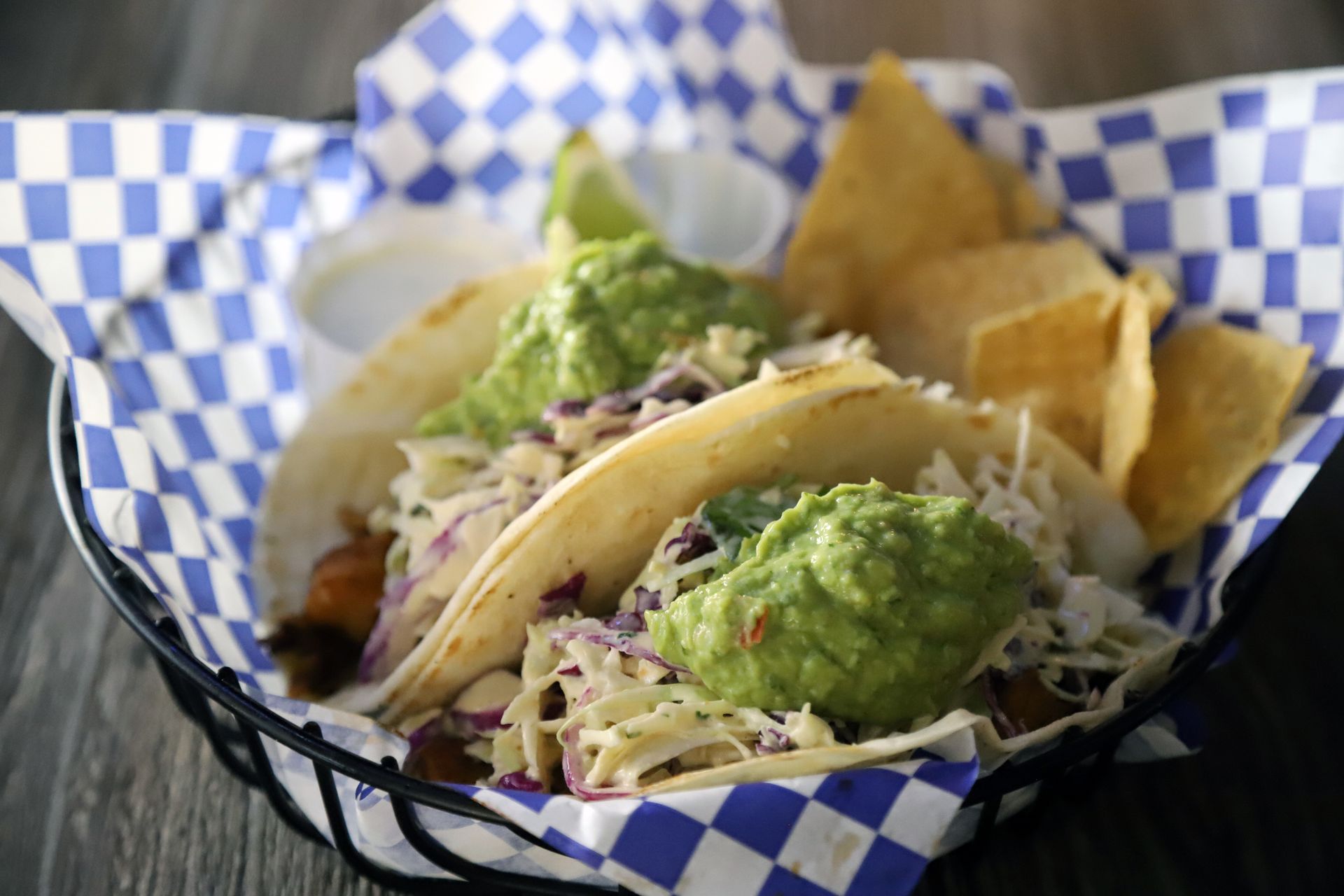 Tacos with guacamole, coleslaw, and chips in a checkered basket.