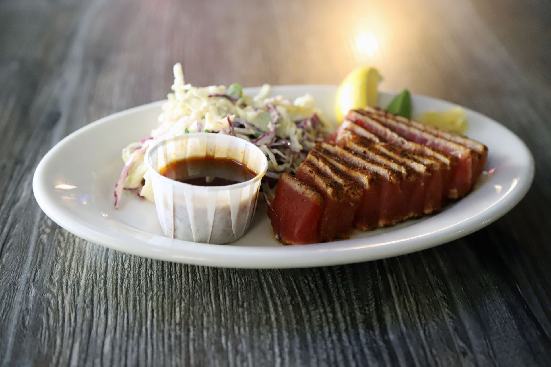 Seared tuna slices with slaw and sauce on a white plate, placed on wood.