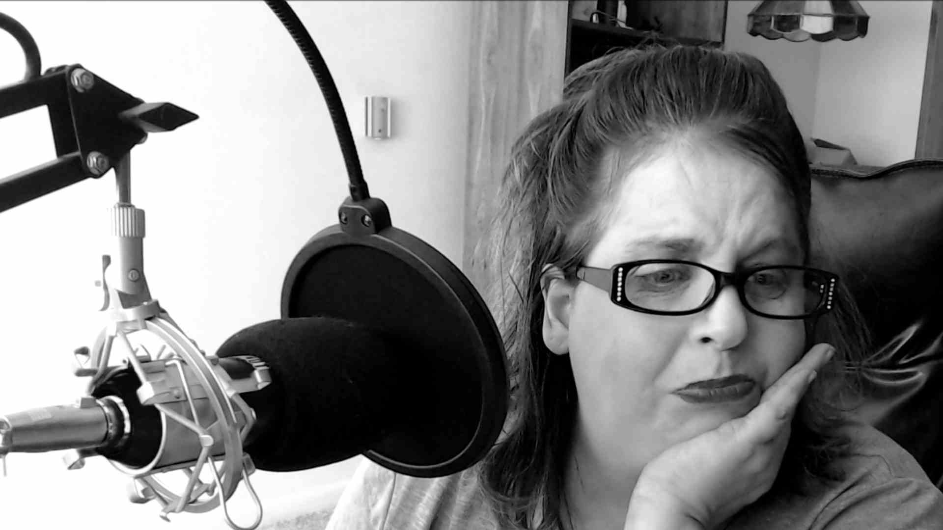 A woman wearing glasses is sitting in front of a microphone.