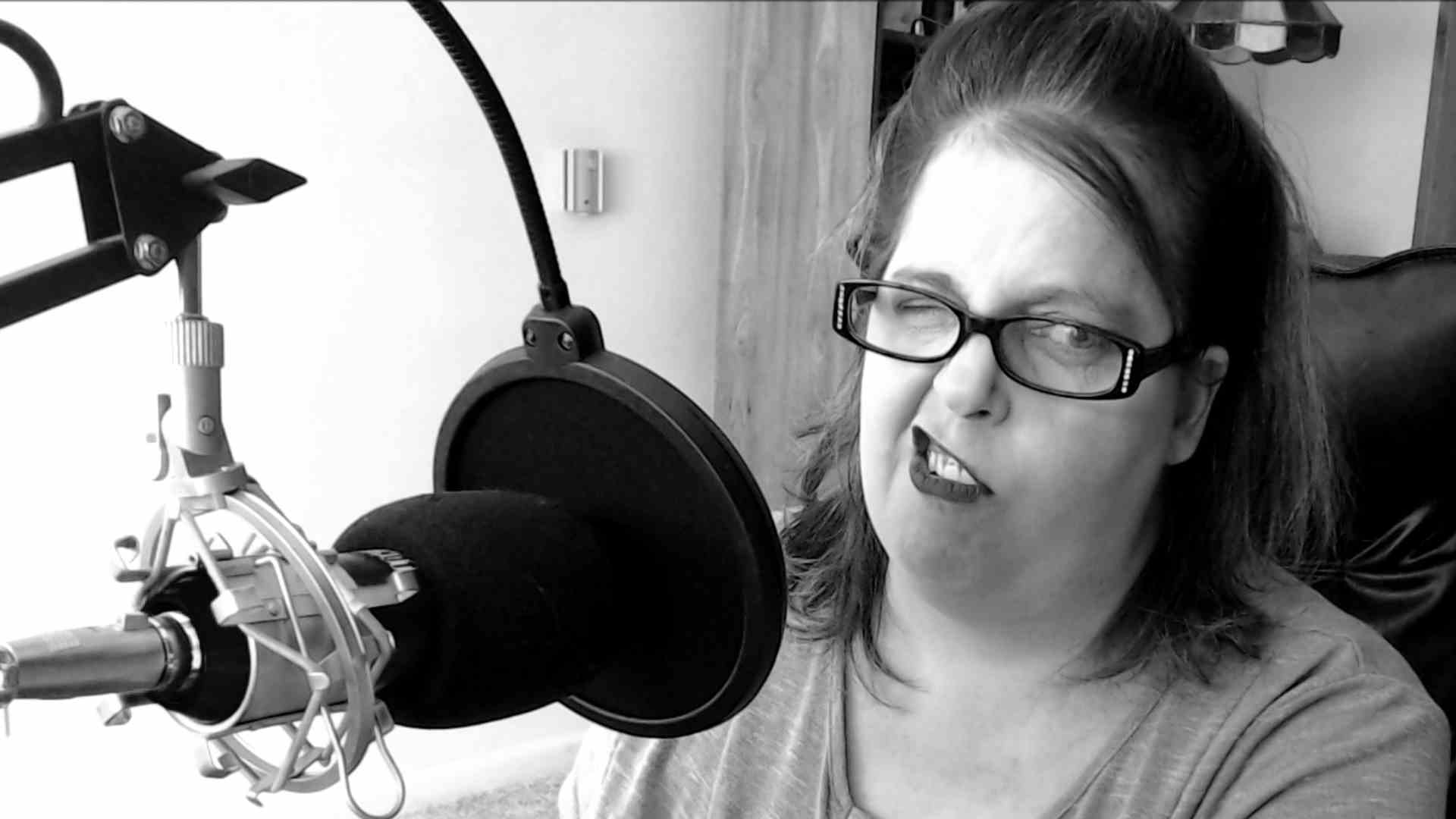A woman wearing glasses is sitting in front of a microphone.