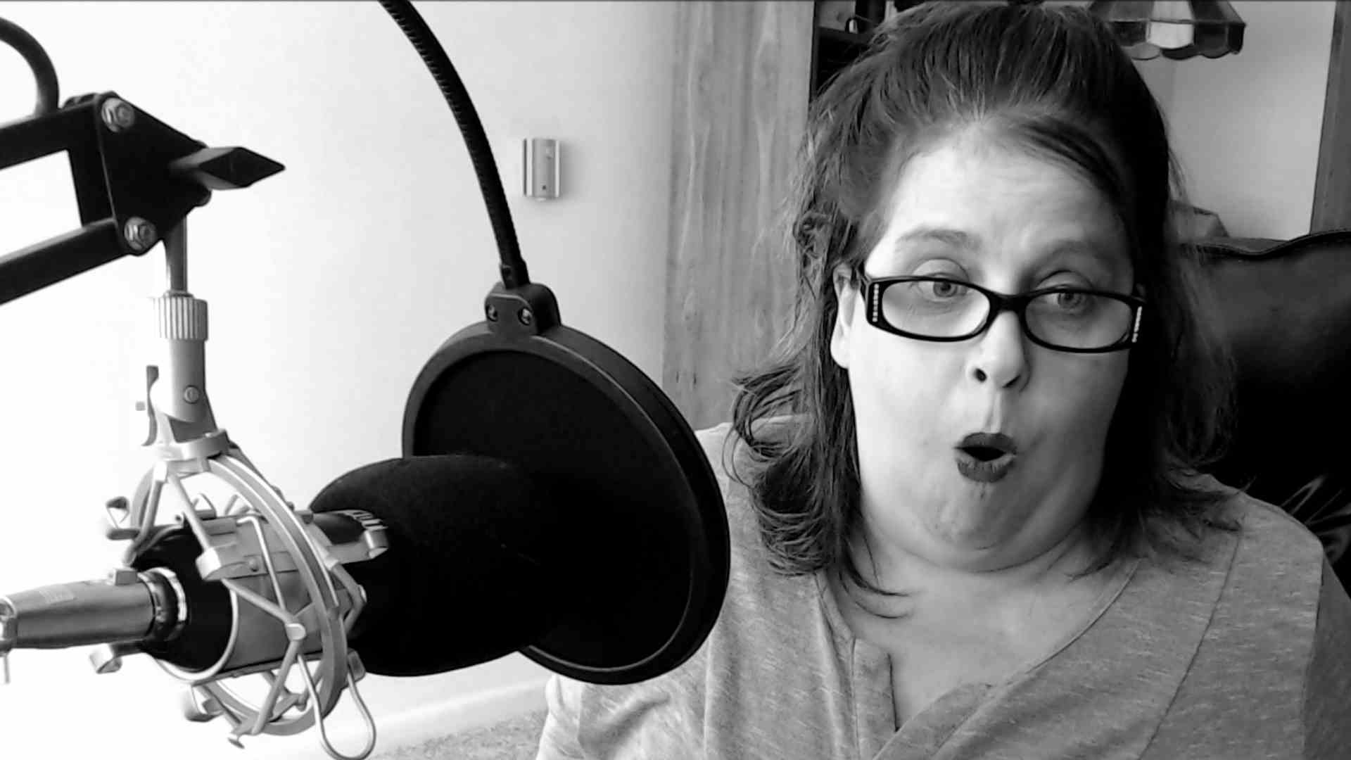A woman wearing glasses is sitting in front of a microphone.